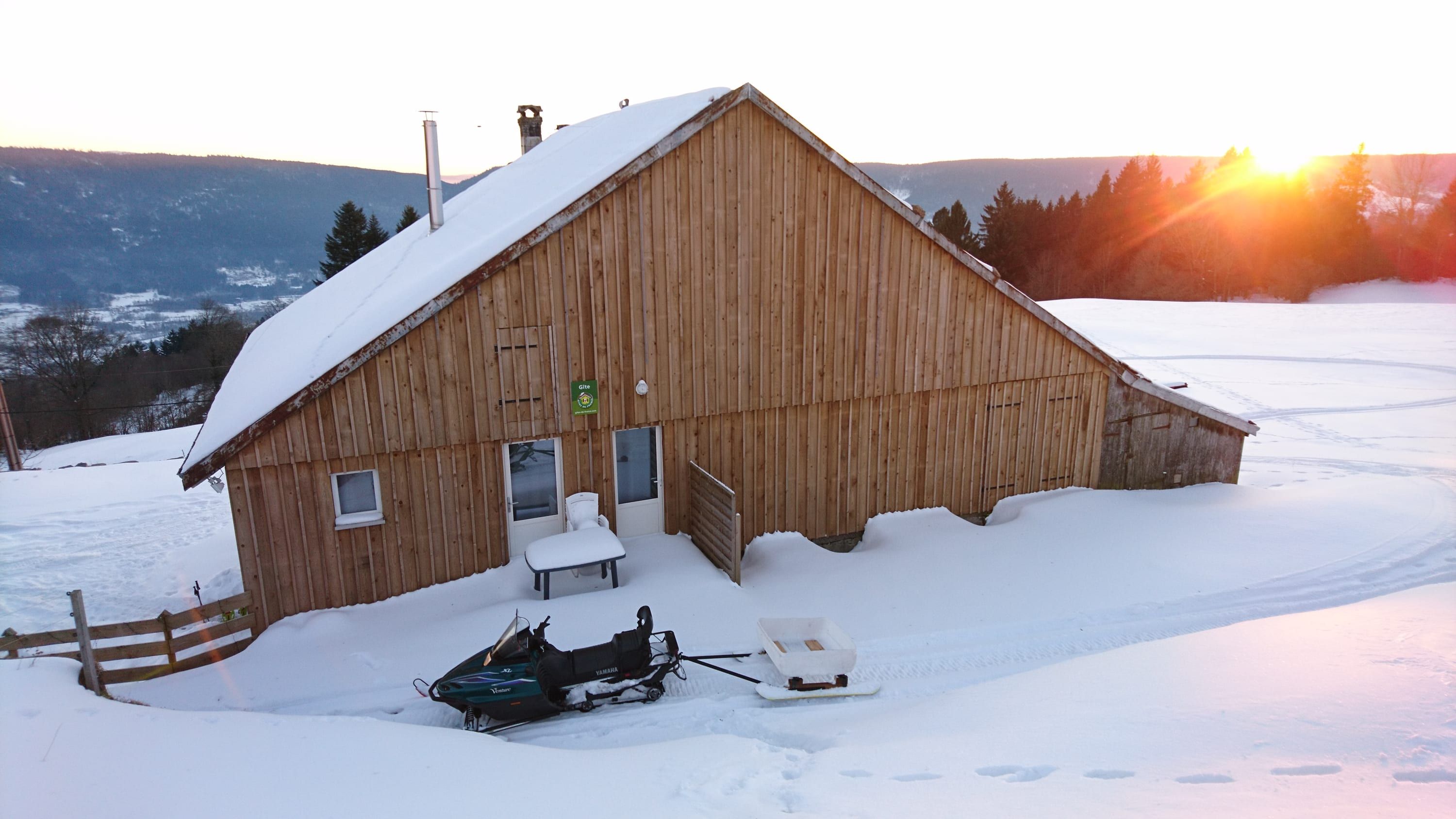 La ferme sous la neige au coucher du soleil, la motoneige devant